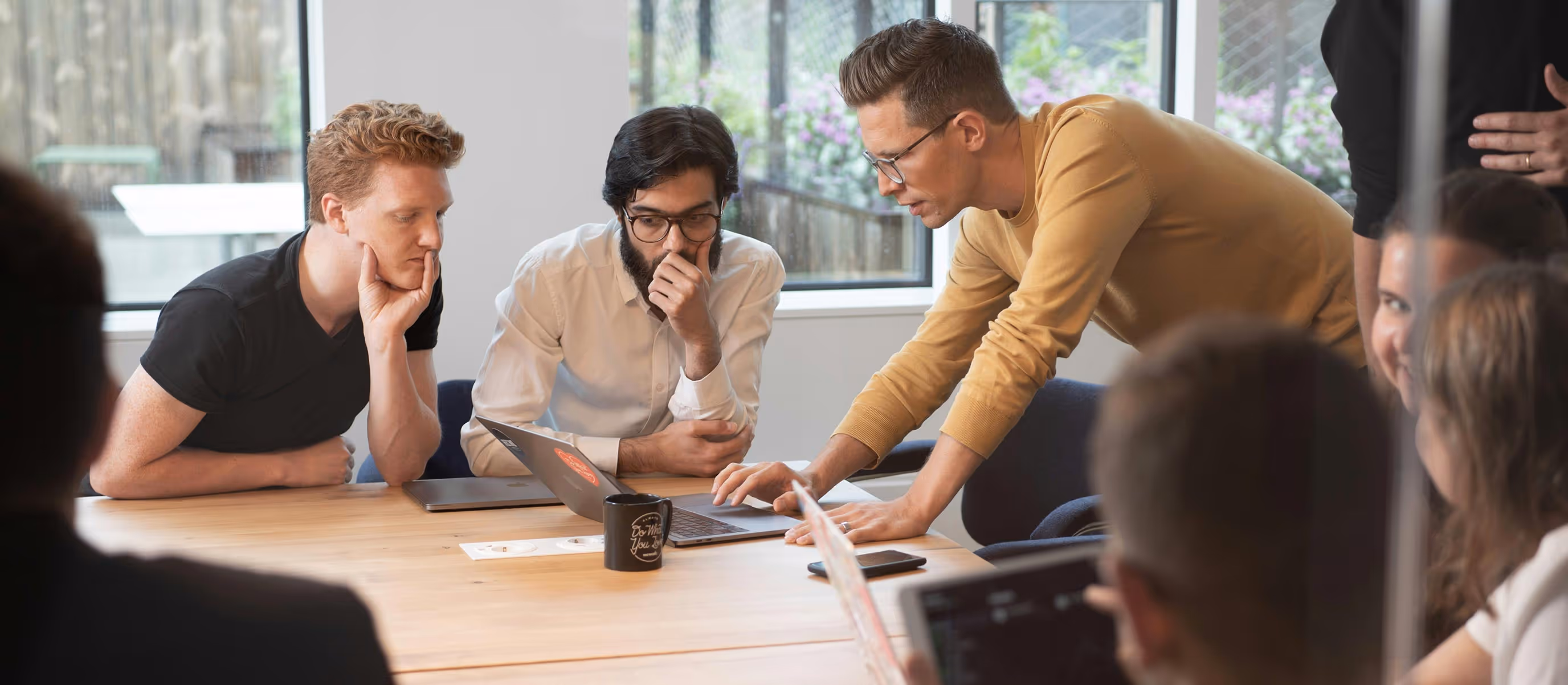 Três pessoas numa sala de reunião, atentas a um portátil, uma delas a apontar para o teclado.